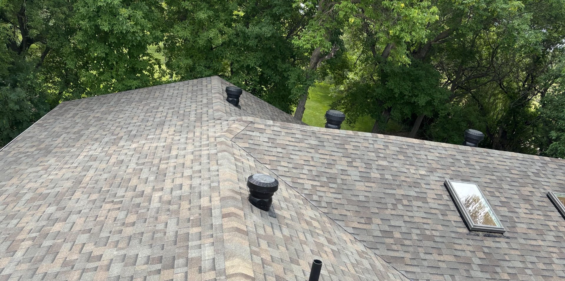 Completed roof with skylight and turbine vents surrounded by green canopy near Canora Saskatchewan
